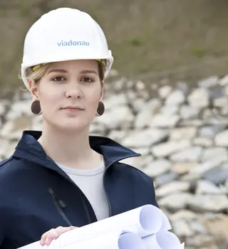 Mitarbeiterin mit Schutzhelm und Planrollen in den Händen