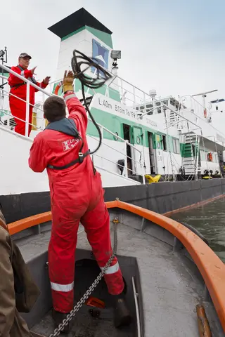 Matrose wirft Tau vom Ufer ans Schiffsdeck