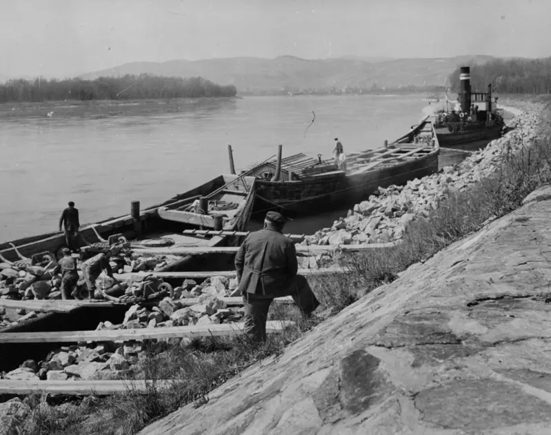 Von Zillen aus tragen Arbeiter große Steine ans Flussufer