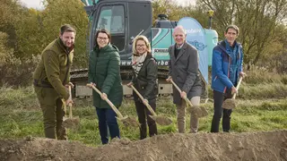 Gruppe mit Spaten vor Bagger