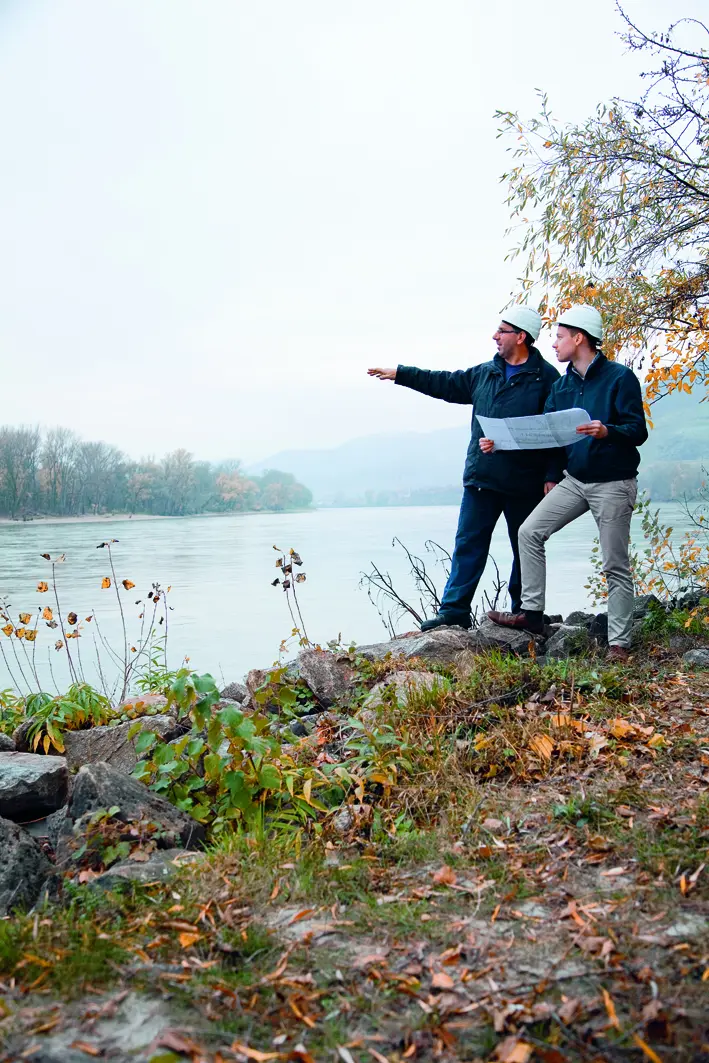 Zwei Mitarbeiter am Donauufer blicken über den Fluss